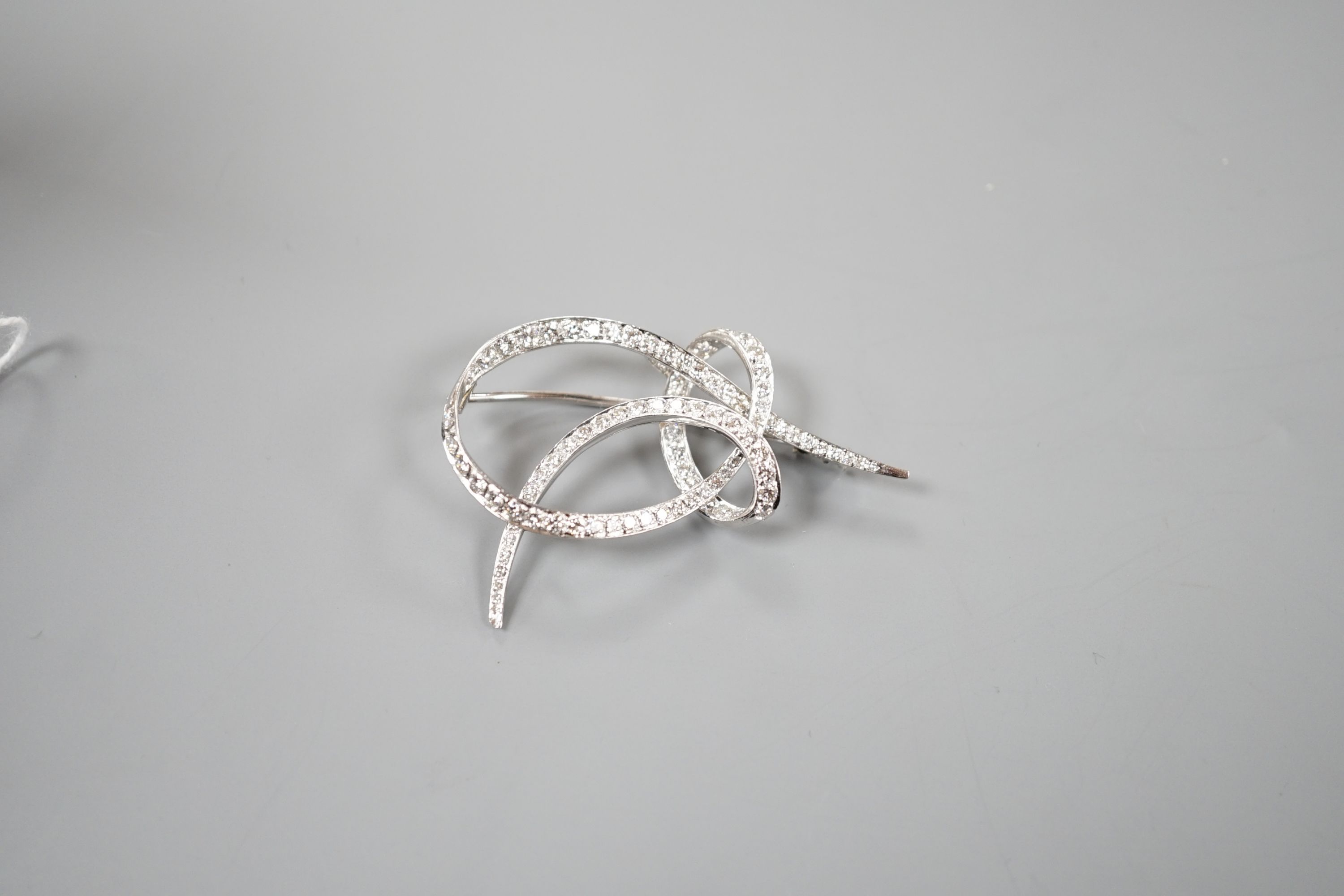 A white metal and diamond cluster set scroll brooch, 52mm, gross weight 14 grams.